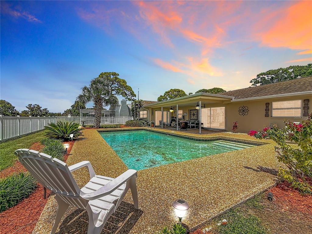 A backyard features a swimming pool with a textured deck and a covered patio area — 6490 BURNING TREE DRIVE, SEMINOLE, FL