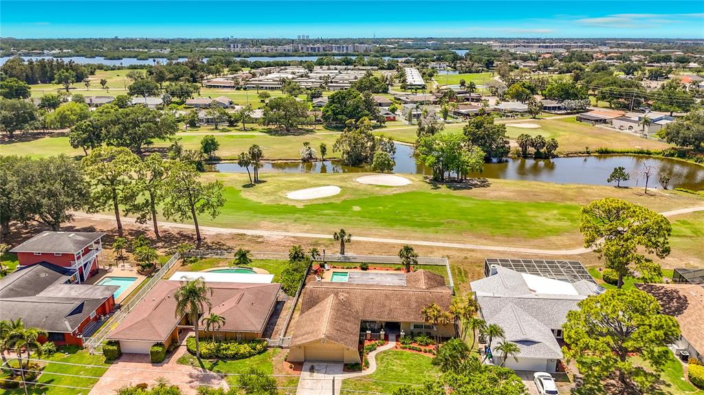 An aerial view shows several suburban houses bordering a golf course with a pond — 6490 BURNING TREE DRIVE, SEMINOLE, FL