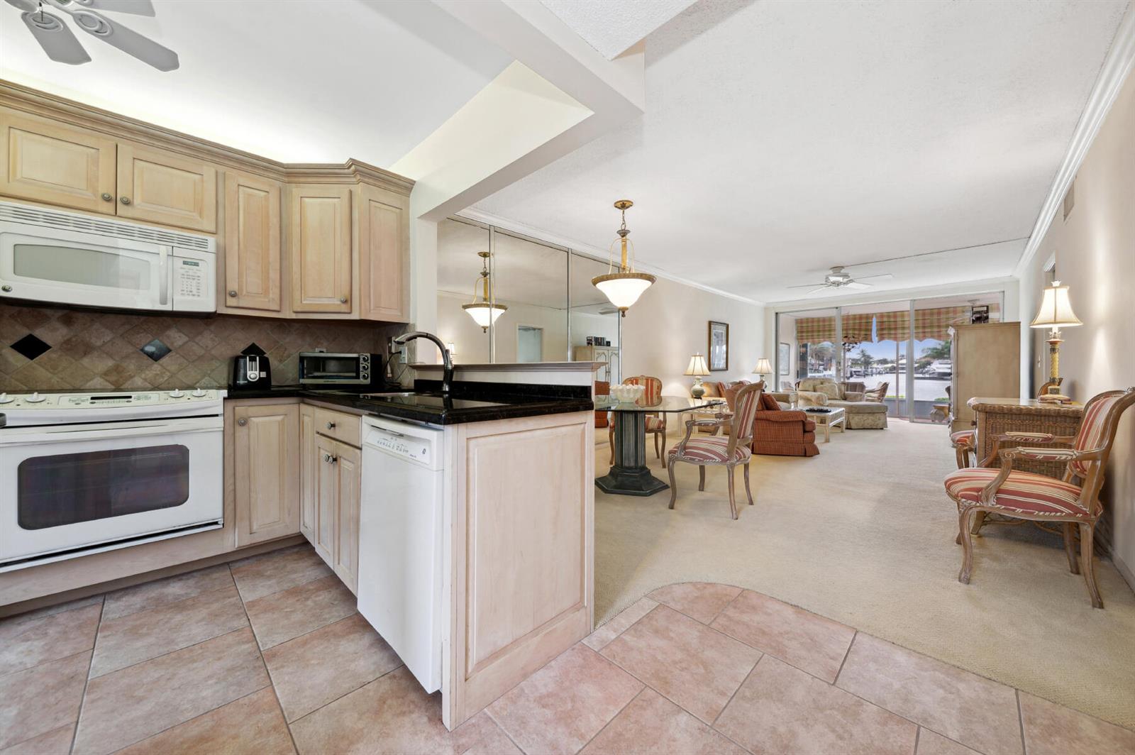 A kitchen with light wood cabinets and tile flooring opens into a carpeted dining area — 3100 S Ocean Boulevard # 116, Highland Beach FL 33487, HIGHLAND BEACH, FL