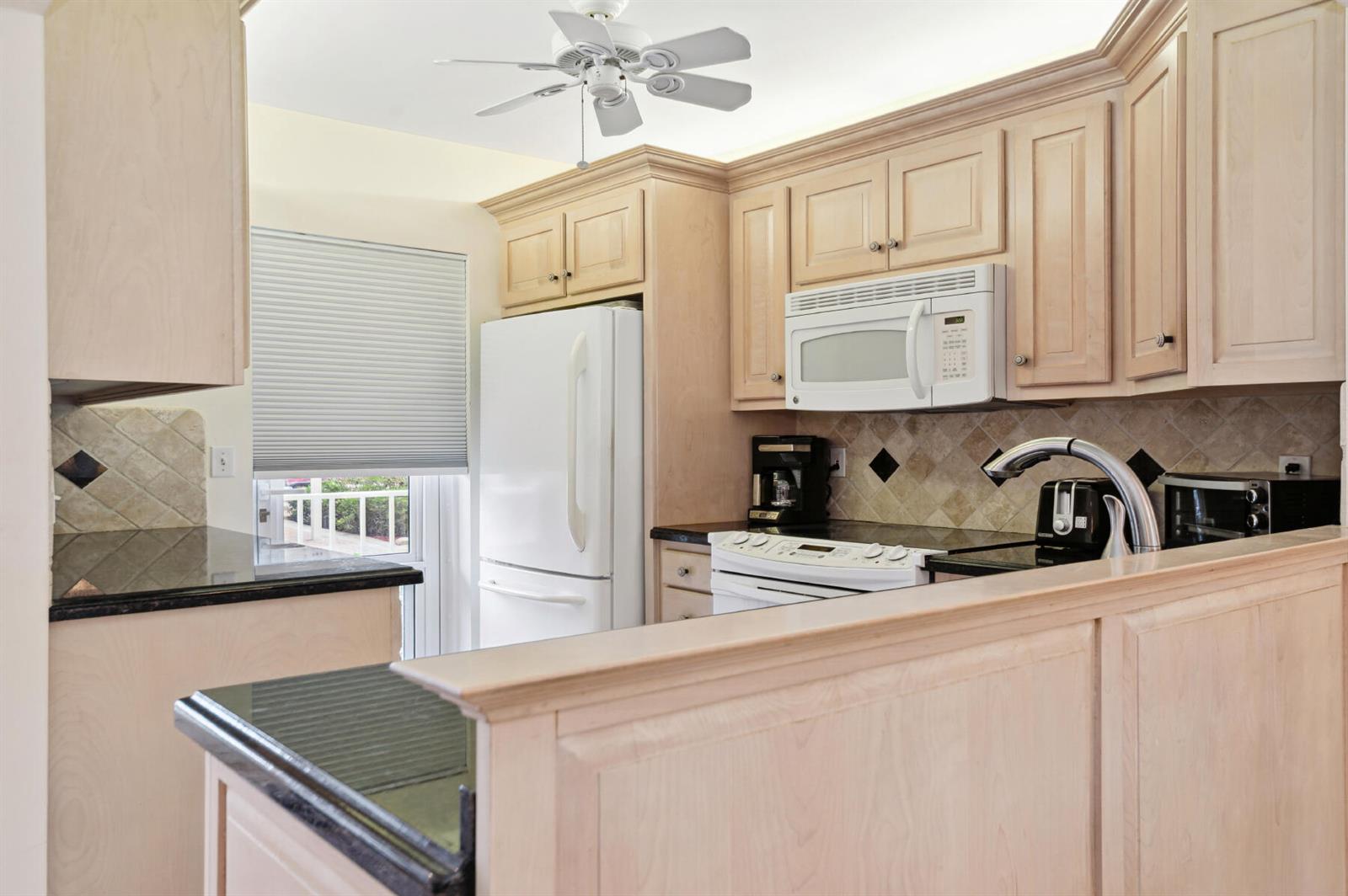 A kitchen with light wood cabinets, black countertops, white appliances, and a ceiling fan — 3100 S Ocean Boulevard # 116, Highland Beach FL 33487, HIGHLAND BEACH, FL