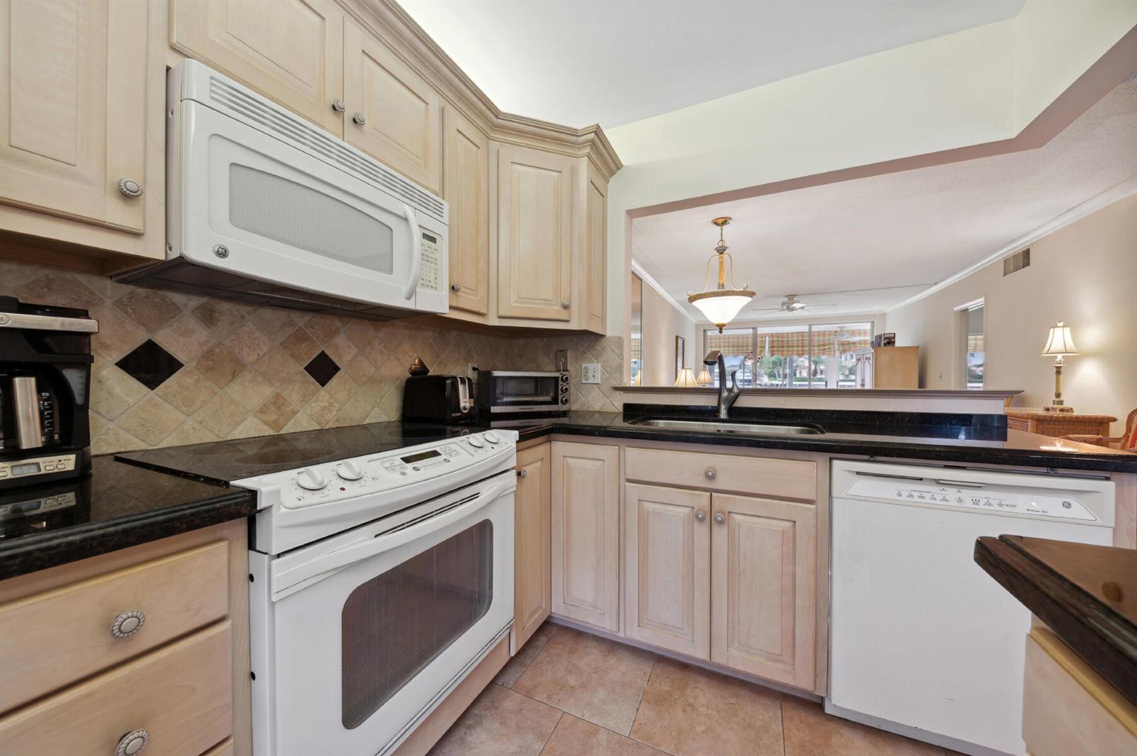 A kitchen features light wood cabinets, black countertops, white appliances, and a tiled backsplash — 3100 S Ocean Boulevard # 116, Highland Beach FL 33487, HIGHLAND BEACH, FL