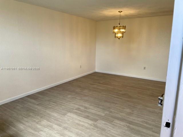 An empty room features light-colored wood-look flooring, plain walls, and a hanging chandelier — 1754 NW 55th Ave # 102, Lauderhill FL 33313, LAUDERHILL, FL