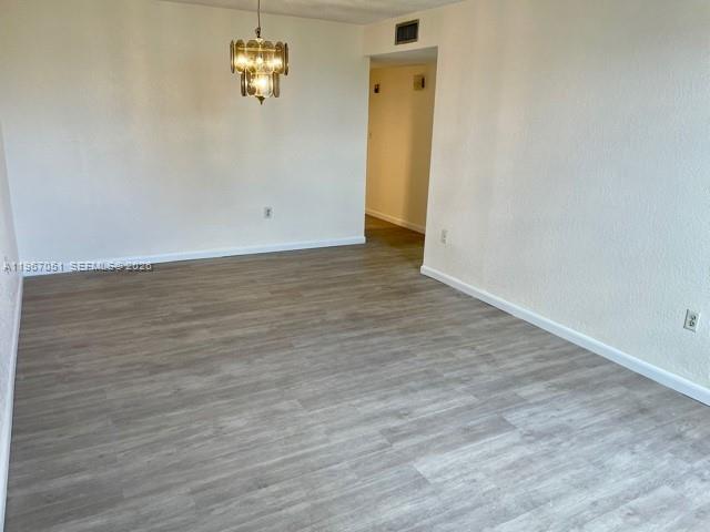 An empty room features light wood-look flooring, white walls, and a hanging chandelier — 1754 NW 55th Ave # 102, Lauderhill FL 33313, LAUDERHILL, FL