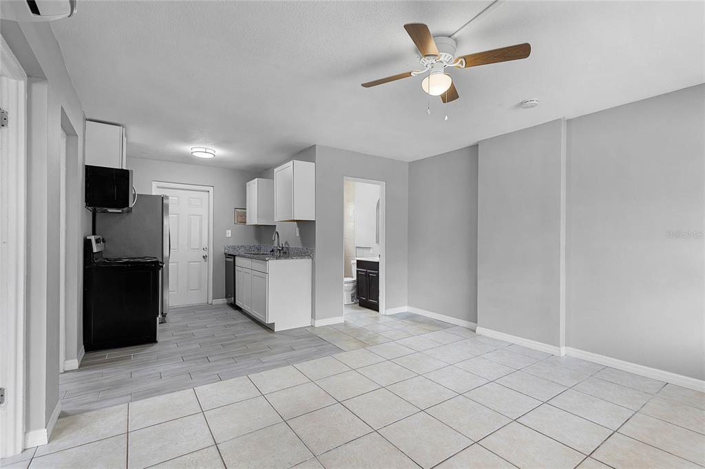 A kitchen with white cabinets and gray tile flooring opens into a tiled living area — 1086 HIBISCUS COURT UNIT 22, TAVARES, FL