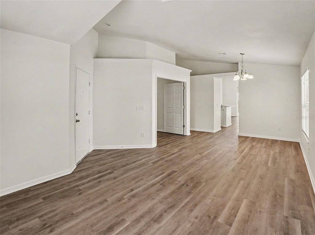 An empty room with light wood-look flooring, white walls, and a vaulted ceiling — 447 LANCER OAK DRIVE, APOPKA, FL