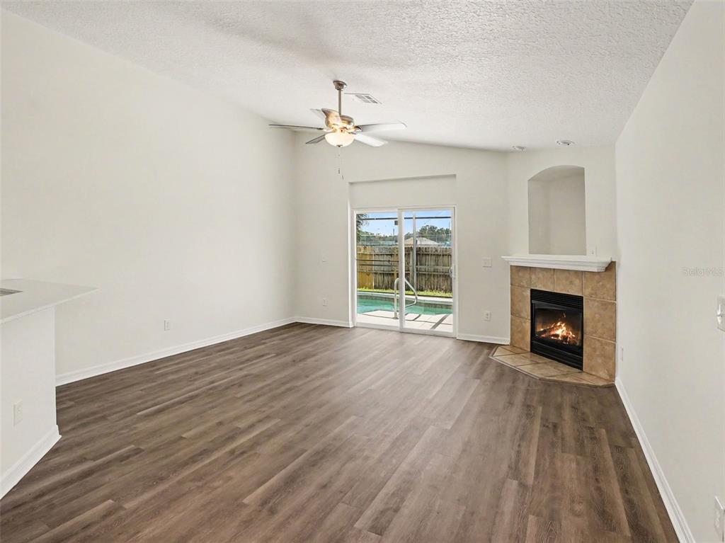 A living room with wood-look flooring, a corner fireplace, and sliding glass doors to a pool — 447 LANCER OAK DRIVE, APOPKA, FL