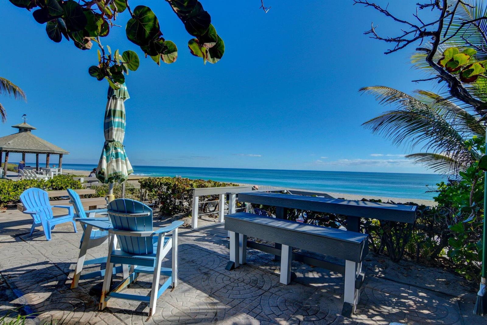 A patio with blue chairs and a picnic table overlooks the ocean and beach — 5550 N Ocean Boulevard # 107, Ocean Ridge FL 33435, OCEAN RIDGE, FL
