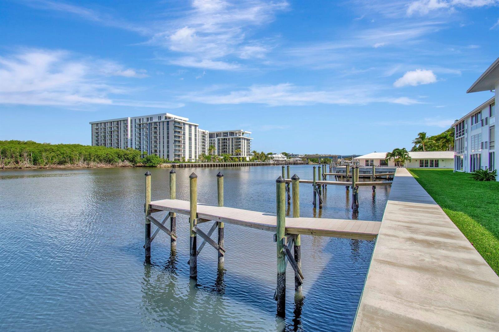 A concrete walkway leads to a wooden boat dock on a calm canal near buildings — 5550 N Ocean Boulevard # 107, Ocean Ridge FL 33435, OCEAN RIDGE, FL