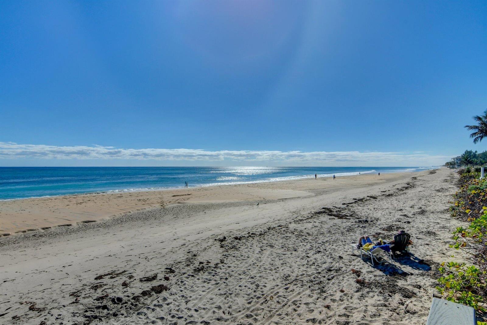 A sandy beach stretches along the ocean with a few people walking and sitting nearby — 5550 N Ocean Boulevard # 107, Ocean Ridge FL 33435, OCEAN RIDGE, FL