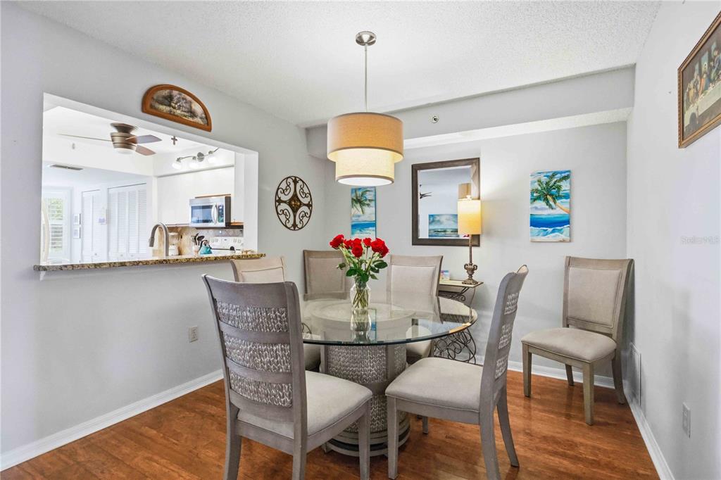 A dining area features a glass-topped table, four upholstered chairs, and a pass-through kitchen window — 7301 29TH AVENUE DR W UNIT 105, BRADENTON, FL