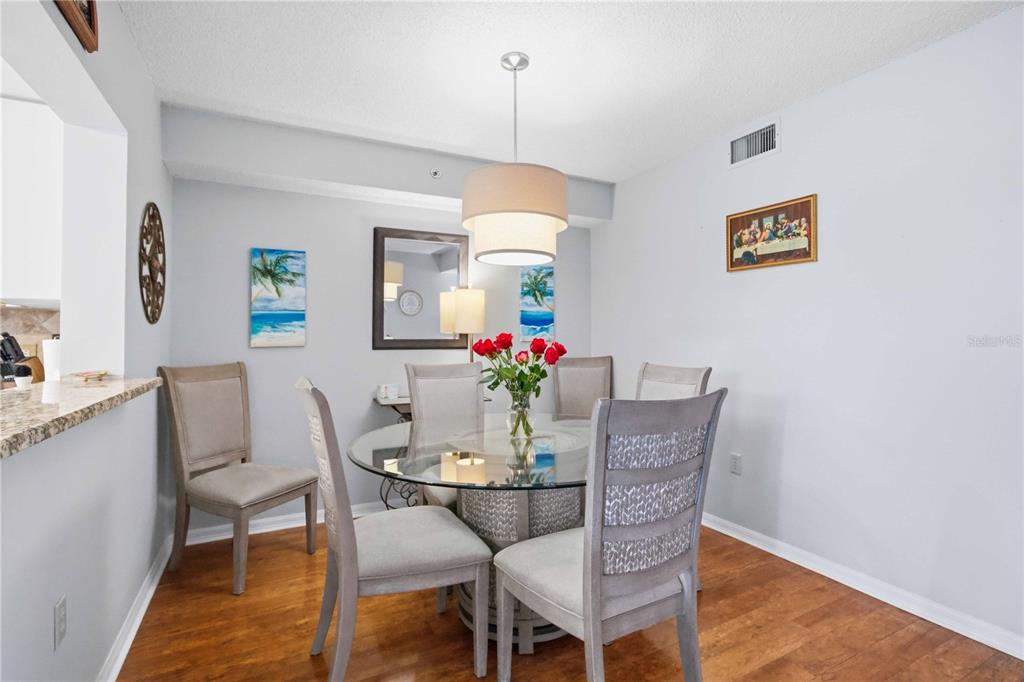 A dining room features a glass-topped table, six upholstered chairs, and a drum pendant light — 7301 29TH AVENUE DR W UNIT 105, BRADENTON, FL
