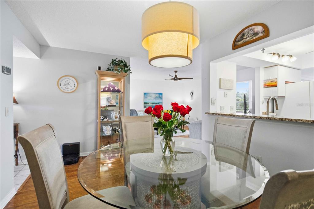 A dining area features a glass-topped table with roses, upholstered chairs, and a pendant light — 7301 29TH AVENUE DR W UNIT 105, BRADENTON, FL