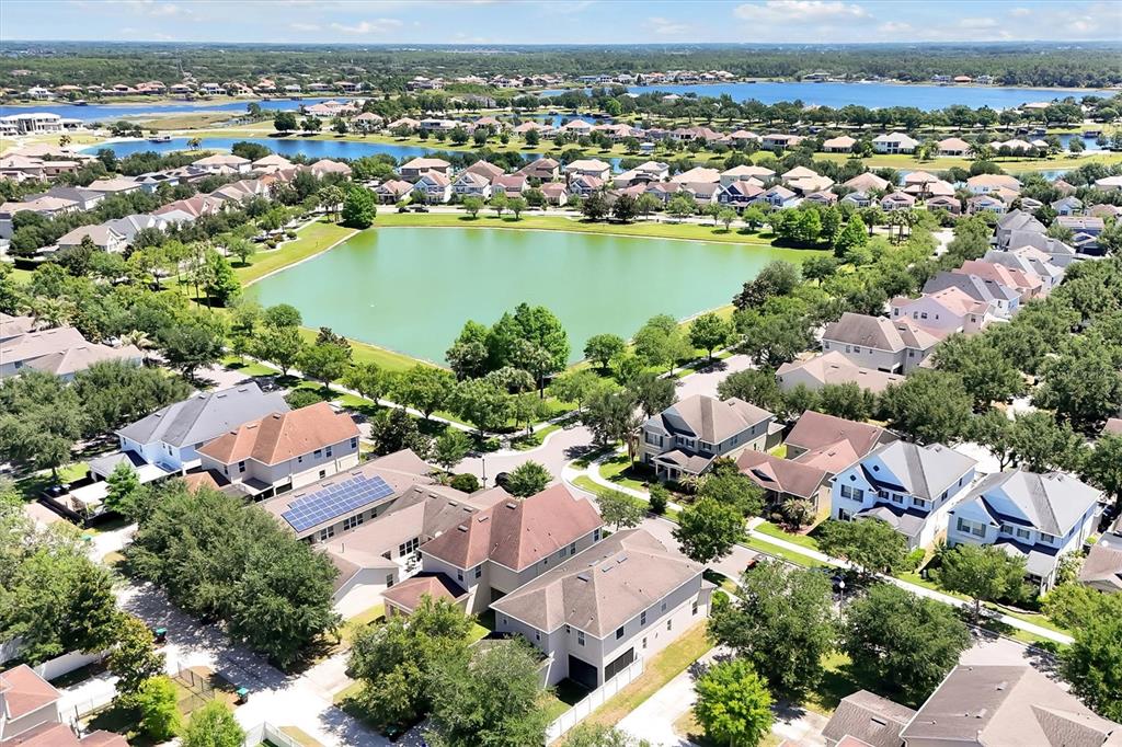 An aerial view shows a suburban neighborhood with houses surrounding a central pond — 7922 WINTER WREN STREET, WINTER GARDEN, FL