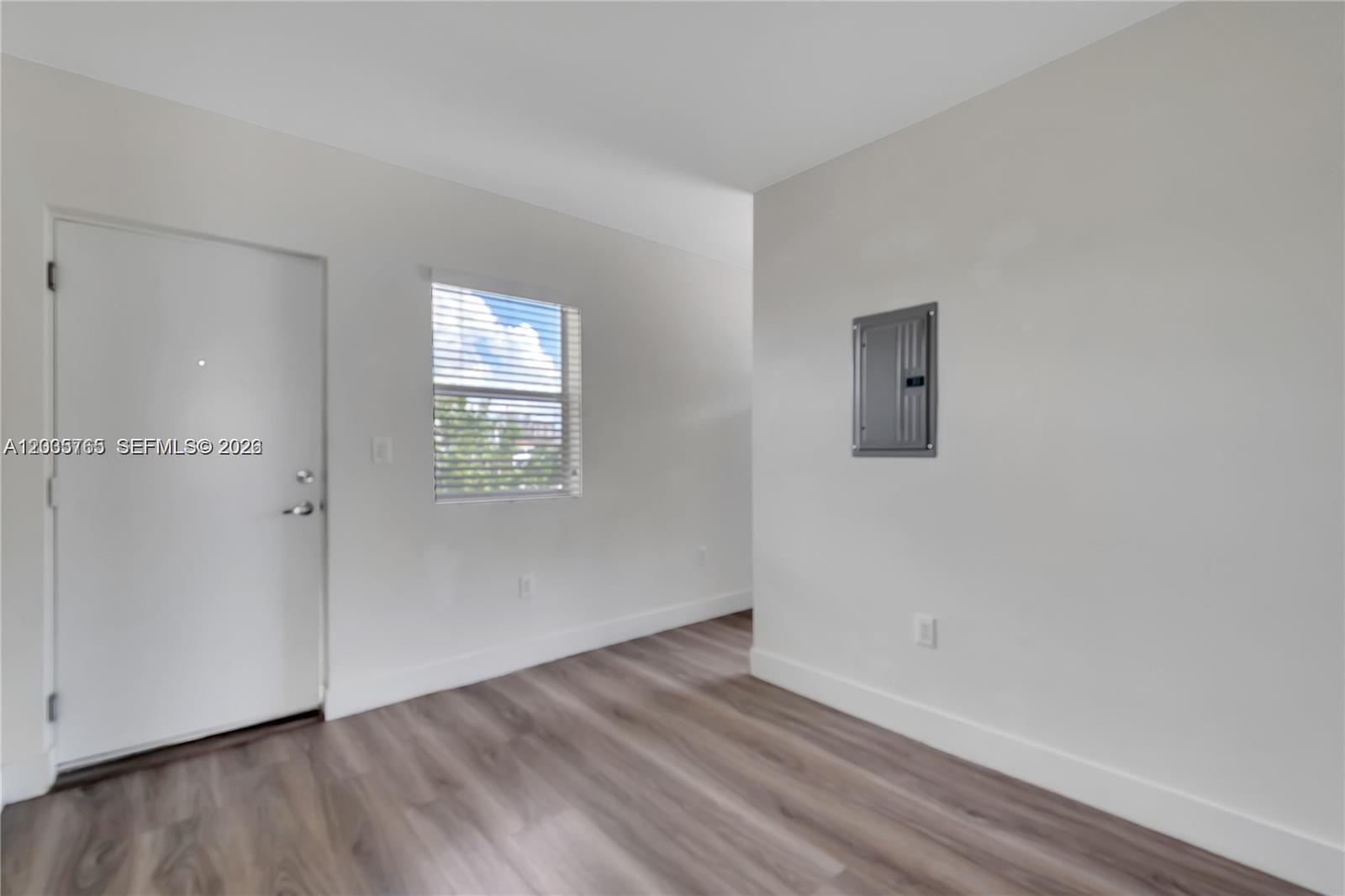 An interior room features white walls, wood-look flooring, a window with blinds, and an electrical panel — 1710 NW 1st Ct # 13, Miami FL 33136, MIAMI, FL
