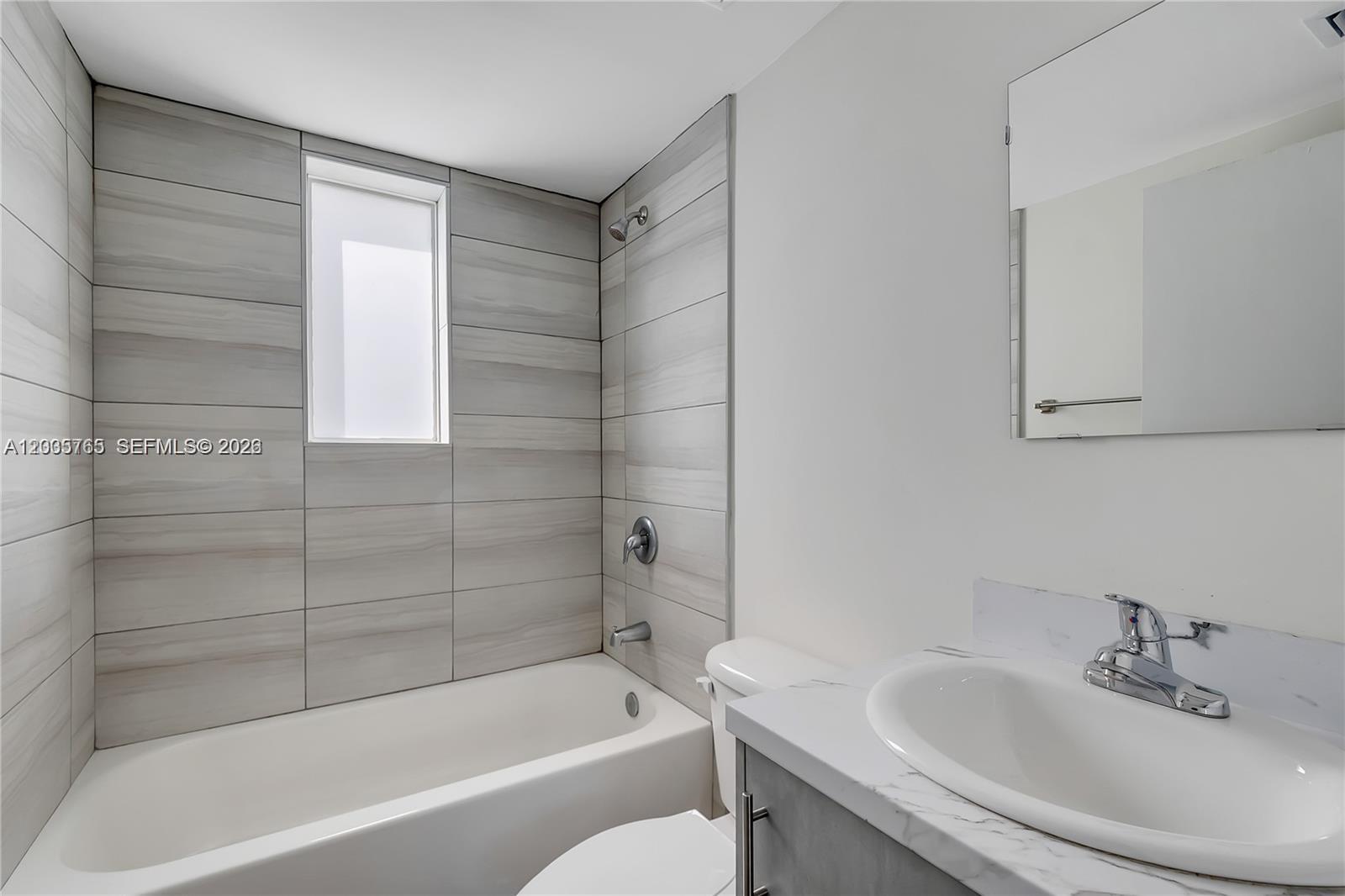A bathroom features a white bathtub, light gray tiled walls, and a marble-topped vanity — 1710 NW 1st Ct # 13, Miami FL 33136, MIAMI, FL
