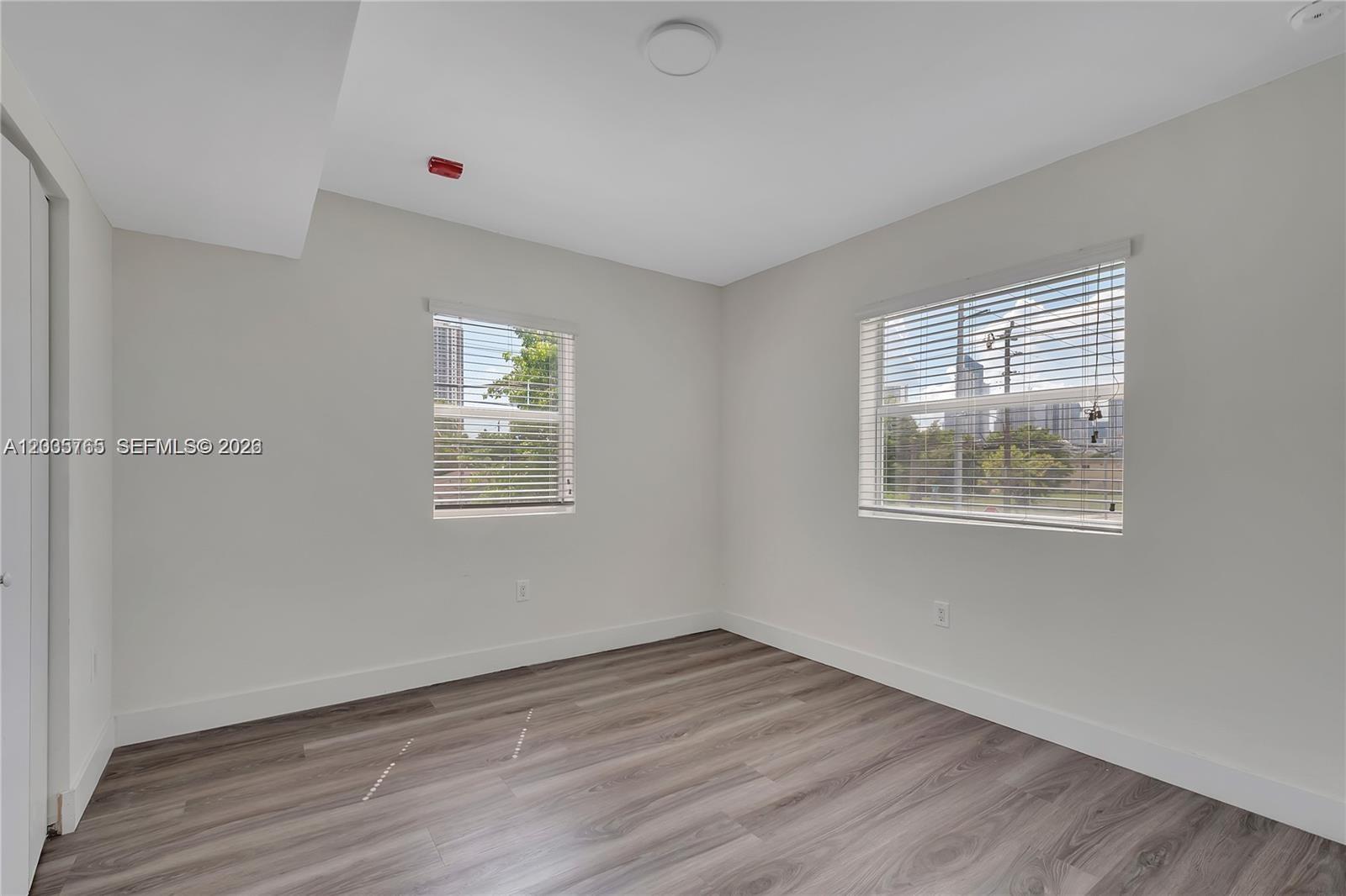 An empty bedroom features light gray walls, wood-look flooring, and two windows with blinds — 1710 NW 1st Ct # 13, Miami FL 33136, MIAMI, FL
