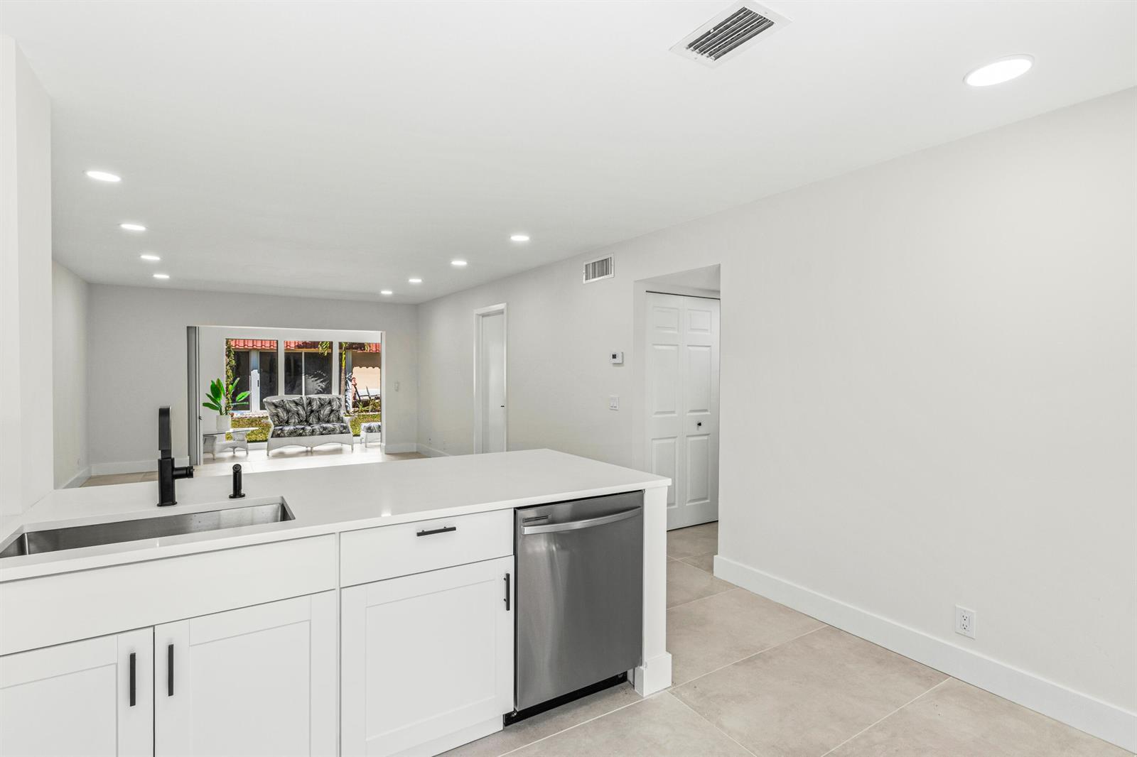 A modern kitchen features white cabinets, a stainless steel dishwasher, and a view of a patio — 733 Nantucket Circle, Lake Worth FL 33467, LAKE WORTH, FL