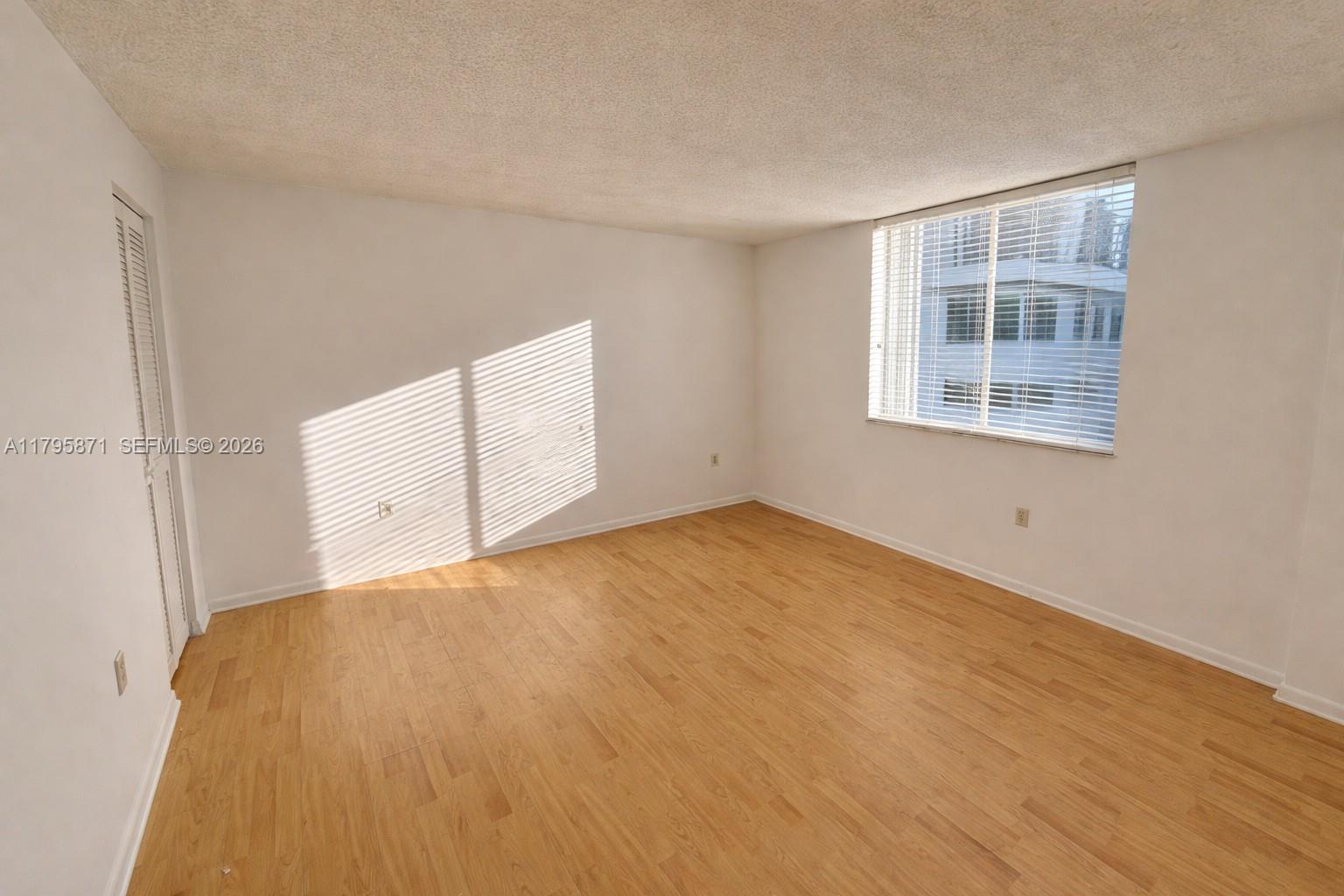 An empty room features light wood-look flooring, white walls, and a window with blinds — 126 SW 17th Rd # 505, Miami FL 33129, MIAMI, FL