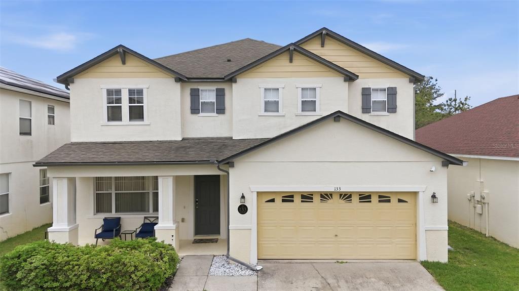 A two-story house with a tan stucco exterior, a front porch, and a two-car garage — 133 BAY LEAF LANE, DAVENPORT, FL