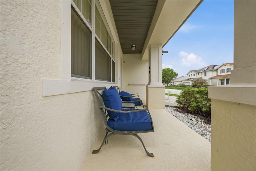 A covered front porch features two chairs with blue cushions and a view of neighborhood homes — 133 BAY LEAF LANE, DAVENPORT, FL