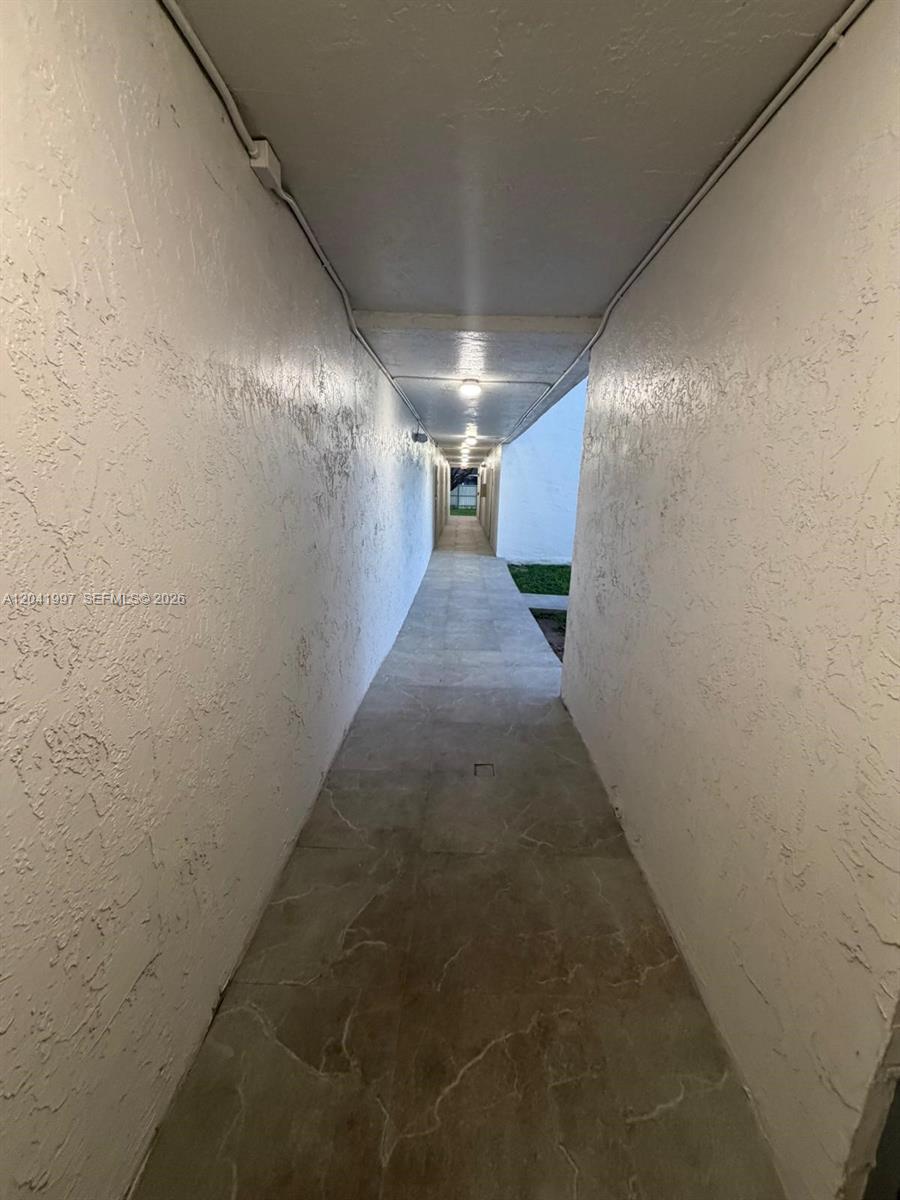 A narrow, covered outdoor walkway with white textured walls and light-colored tiled flooring — 9520 SW 8th St # 121, Miami FL 33174, MIAMI, FL