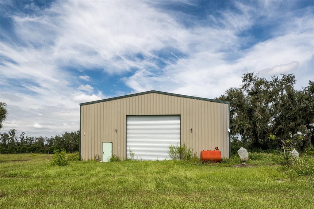 A tan metal warehouse building stands in a grassy field under a blue sky — 32715 SINGLETARY ROAD, MYAKKA CITY, FL