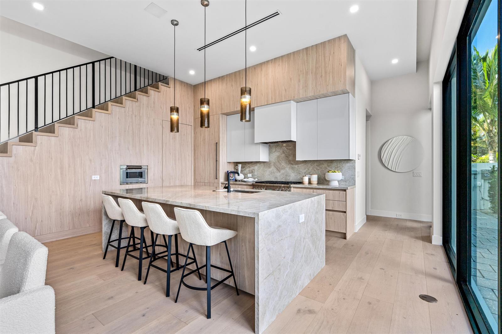 A modern kitchen features a stone waterfall island, light wood cabinetry, and a floating staircase — 723 Lake Avenue N, Delray Beach FL 33483, DELRAY BEACH, FL