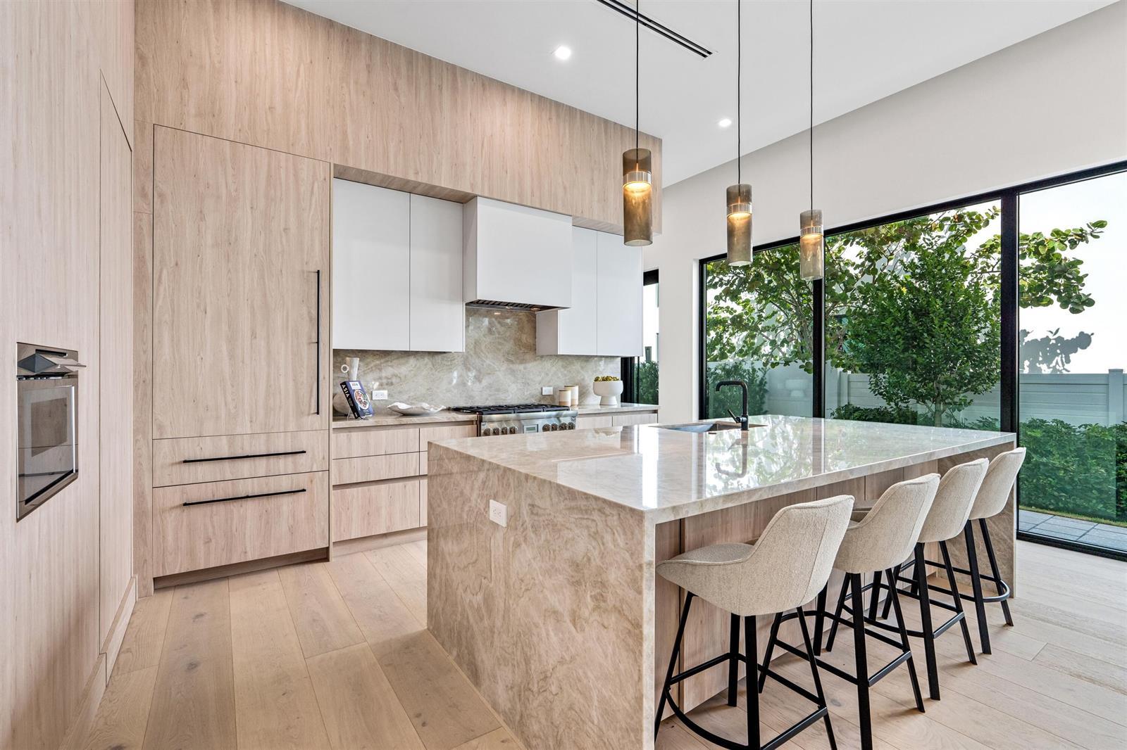 A modern kitchen features light wood cabinetry, a stone island, and large floor-to-ceiling windows — 723 Lake Avenue N, Delray Beach FL 33483, DELRAY BEACH, FL