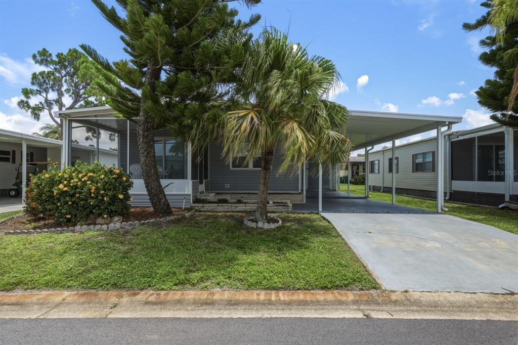 A single-story manufactured home with a screened porch, carport, and palm tree in the front yard — 2100 KINGS HIGHWAY UNIT 522, PORT CHARLOTTE, FL