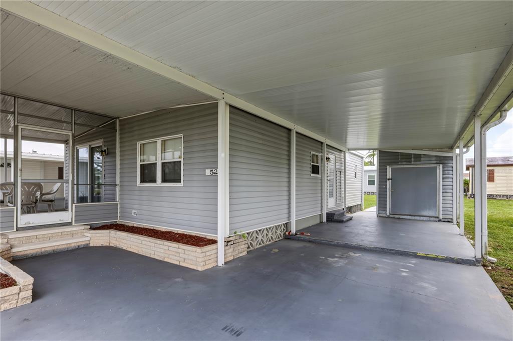 A gray mobile home exterior features a covered carport, a screened porch, and brick planters — 2100 KINGS HIGHWAY UNIT 522, PORT CHARLOTTE, FL