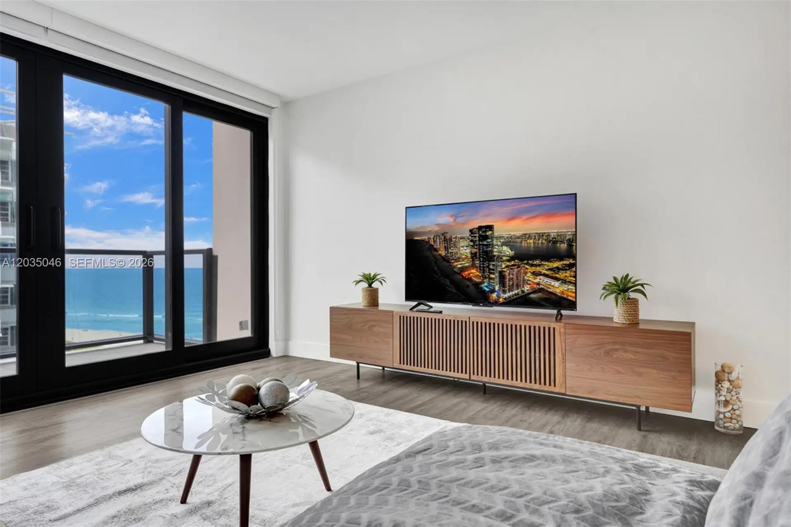 A modern living room features a wood media console, a marble coffee table, and balcony views — 5225 Collins Ave # 1606, Miami Beach FL 33140, MIAMI BEACH, FL
