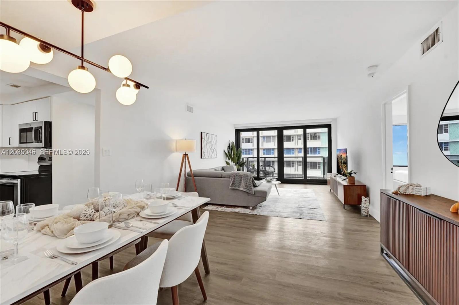 An open-concept living and dining area features white walls, wood-look flooring, and a modern chandelier — 5225 Collins Ave # 1606, Miami Beach FL 33140, MIAMI BEACH, FL