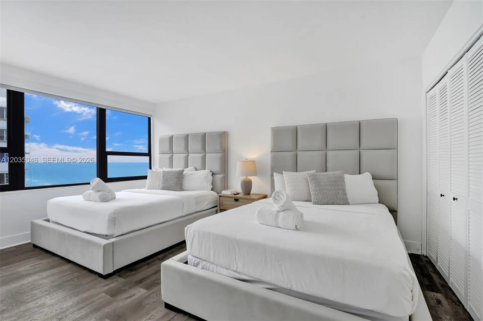 A bedroom features two beds with gray tufted headboards and a large ocean-view window — 5225 Collins Ave # 1606, Miami Beach FL 33140, MIAMI BEACH, FL