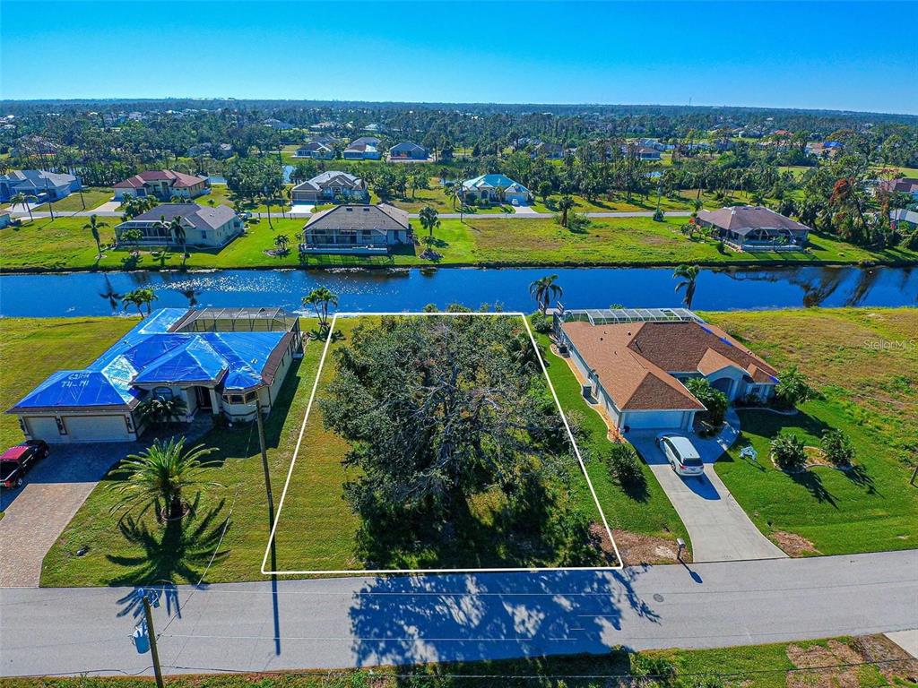 An aerial view shows a vacant residential lot with a large tree between two houses — 34 PINE VALLEY LANE, ROTONDA WEST, FL