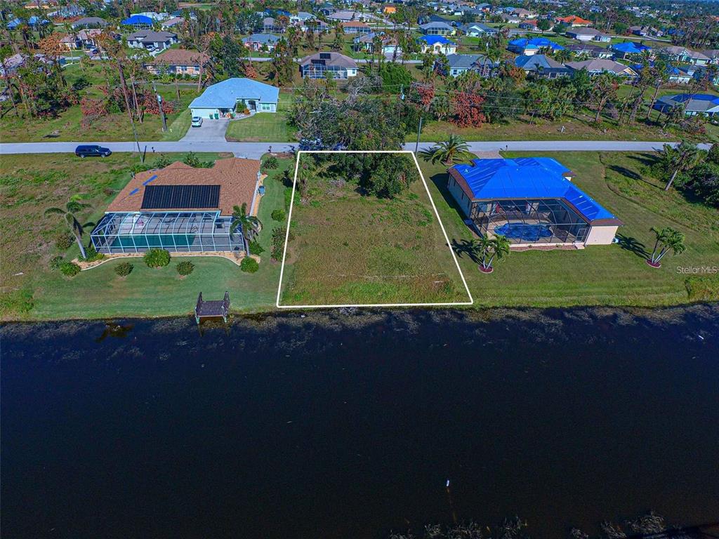 An aerial view shows a vacant waterfront lot situated between two houses with pools — 34 PINE VALLEY LANE, ROTONDA WEST, FL