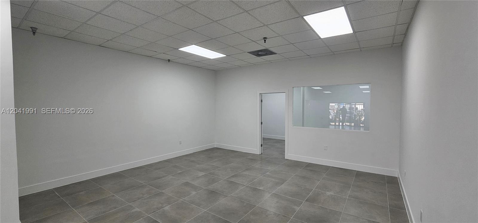 An empty office room features white walls, gray tile flooring, and a drop ceiling — MIAMI, FL