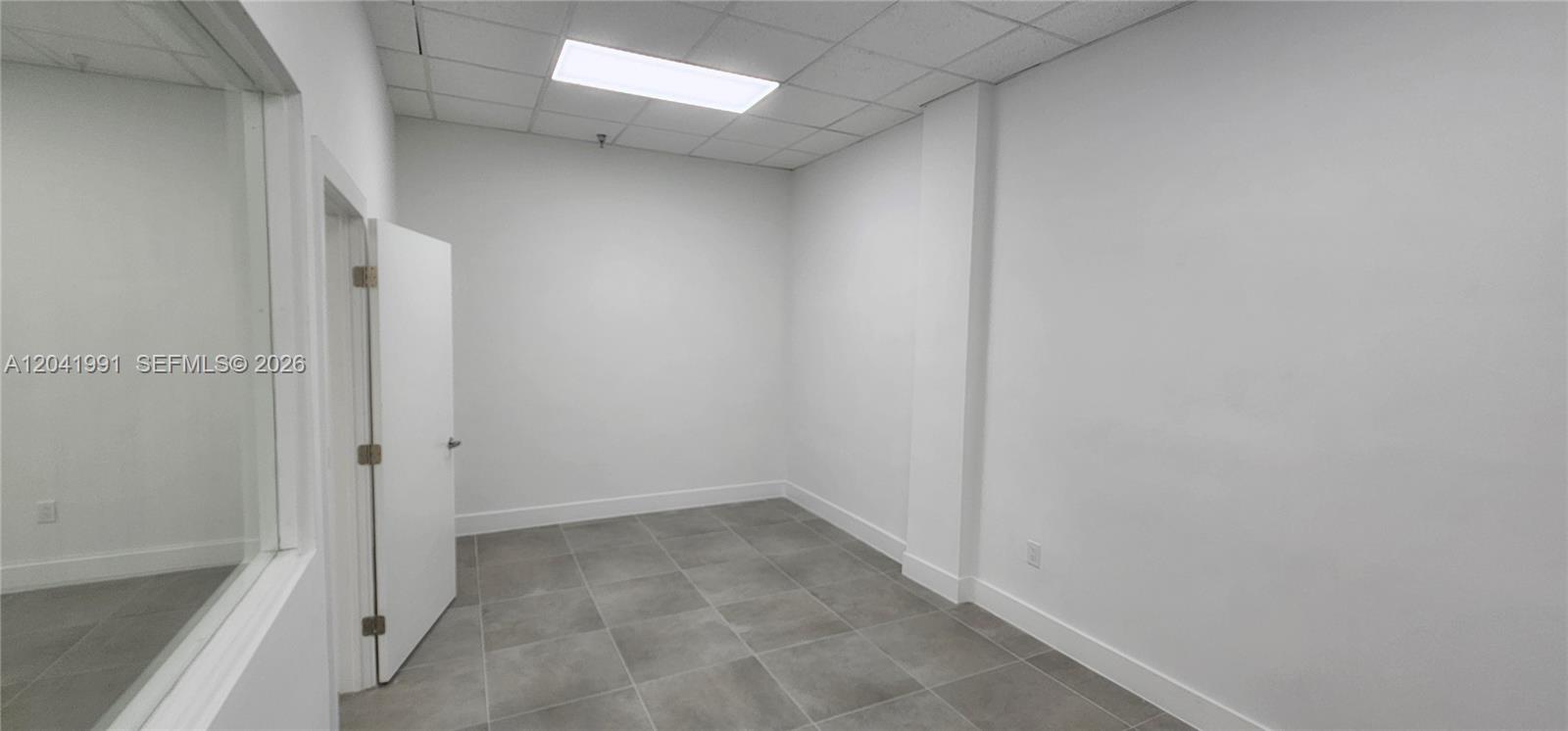 An empty office room features white walls, a drop ceiling, and gray tiled flooring — MIAMI, FL
