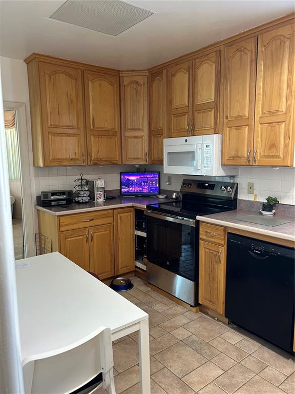 A kitchen features wood cabinets, stainless steel appliances, and a white table on tile flooring — 2201 S PENINSULA DRIVE, DAYTONA BEACH, FL