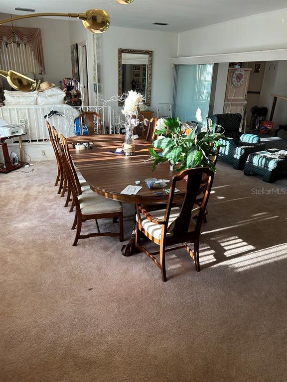 A dining room features a large wooden table, chairs, and a plant on beige carpet — 2201 S PENINSULA DRIVE, DAYTONA BEACH, FL