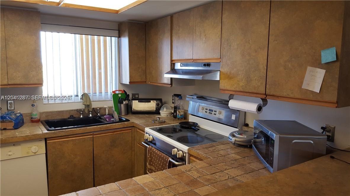 A kitchen features tiled countertops, wooden cabinets, a stove, and a sink by a window — 201 NW 7th St # 408, Miami FL 33136, MIAMI, FL