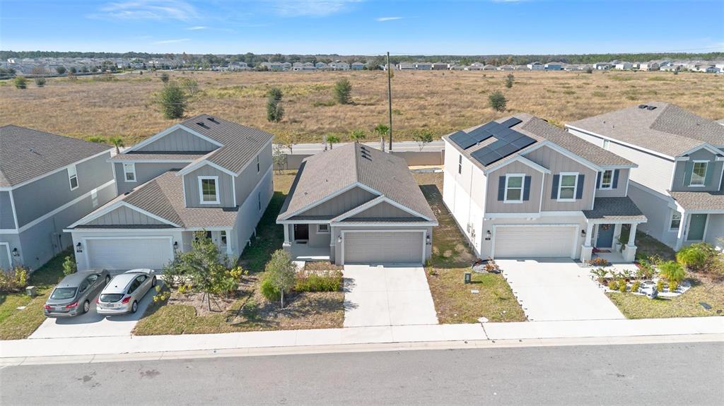 An aerial view shows three suburban houses with driveways and a large field behind them — 360 LOCH CT, DAVENPORT, FL