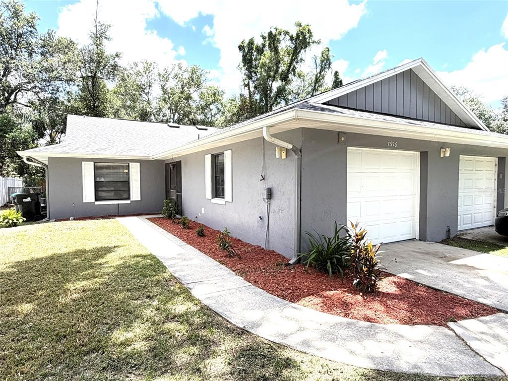 A gray single-story house features a white garage door, a concrete walkway, and red mulch — 7916 RICHWOOD DRIVE, ORLANDO, FL