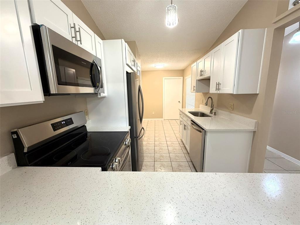 A galley kitchen features white cabinets, stainless steel appliances, and light-colored quartz countertops — 7916 RICHWOOD DRIVE, ORLANDO, FL