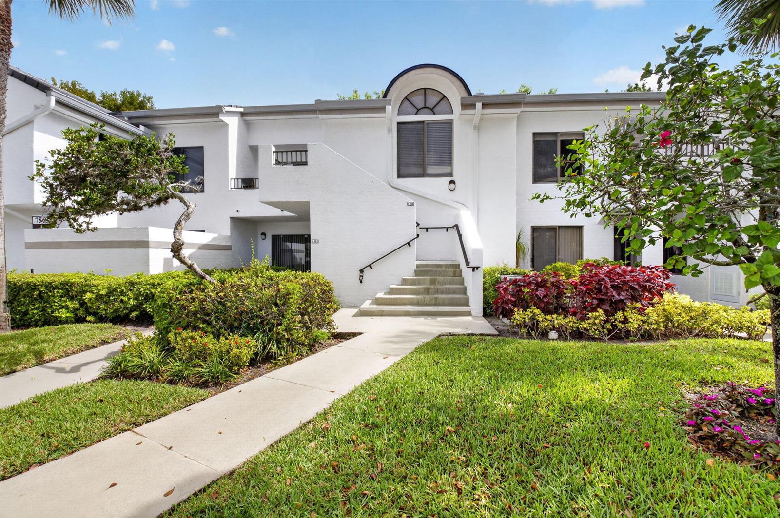 A two-story white stucco building features a central staircase leading to an upper-level entrance — 7563 Glendevon Lane # 1306, Delray Beach FL 33446, DELRAY BEACH, FL
