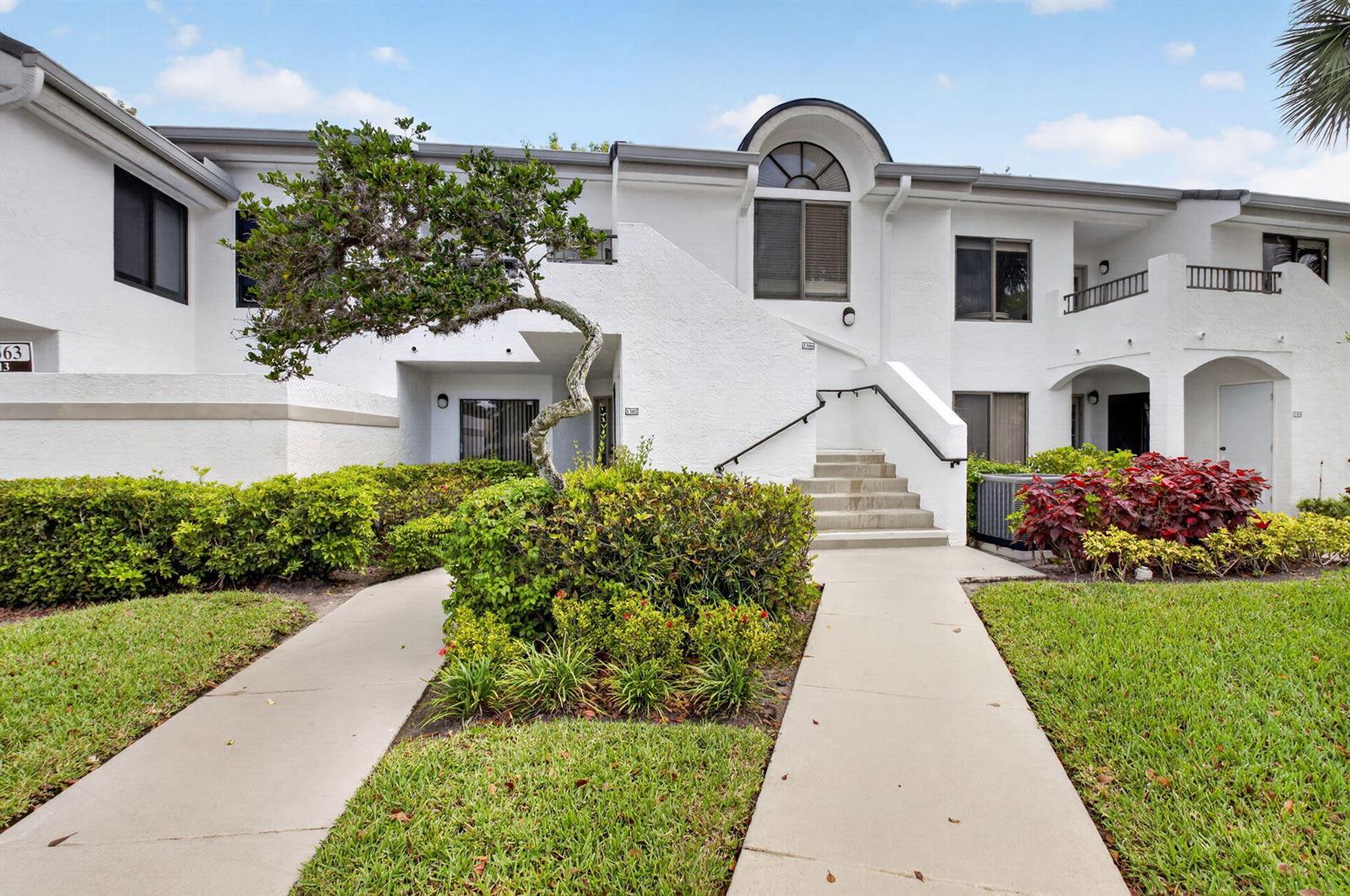 A two-story white stucco building features a curved tree, concrete walkways, and exterior stairs — 7563 Glendevon Lane # 1306, Delray Beach FL 33446, DELRAY BEACH, FL