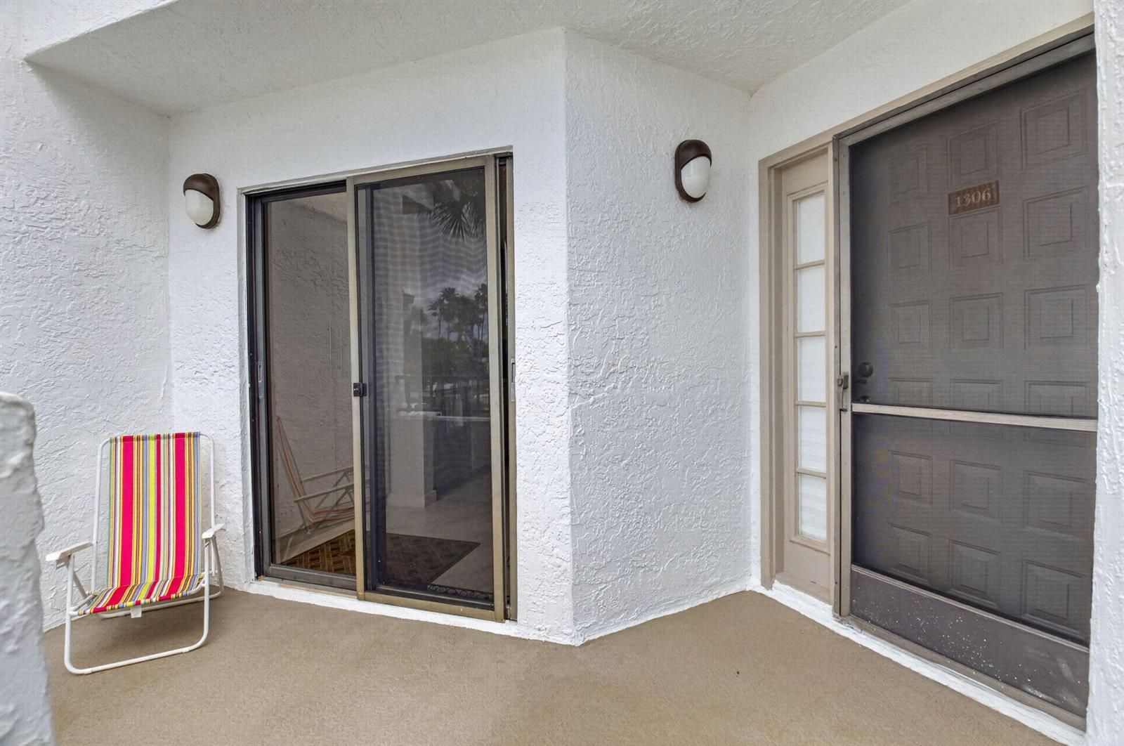 A patio features a striped folding chair, a sliding glass door, and a screen door — 7563 Glendevon Lane # 1306, Delray Beach FL 33446, DELRAY BEACH, FL