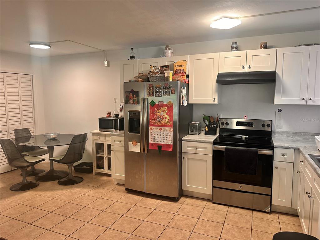 A kitchen features white cabinets, stainless steel appliances, a glass dining table, and tiled flooring — 2938 CLARK ROAD UNIT 102, SARASOTA, FL