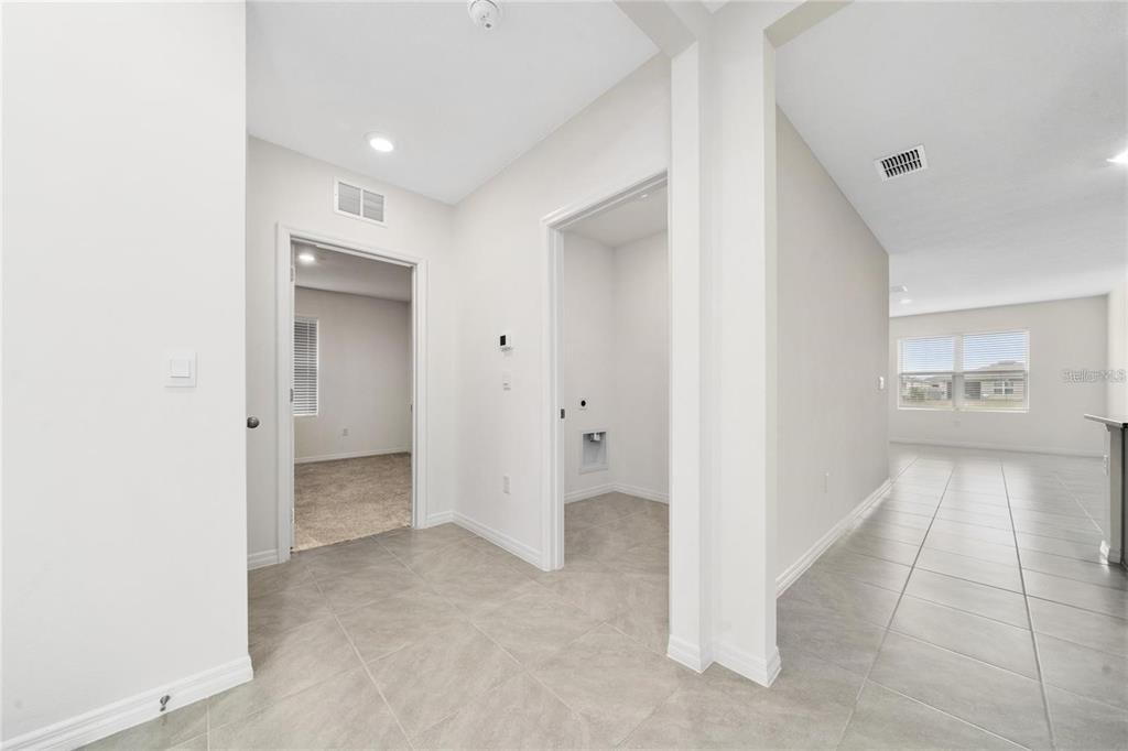 A hallway with tile flooring leads to a carpeted bedroom and a laundry room — 1213 RED HILL ROAD, DAVENPORT, FL