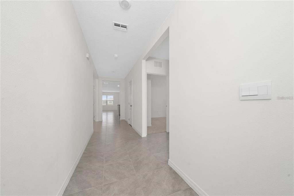 A hallway with light-colored tile flooring leads toward a windowed room in the distance — 1213 RED HILL ROAD, DAVENPORT, FL