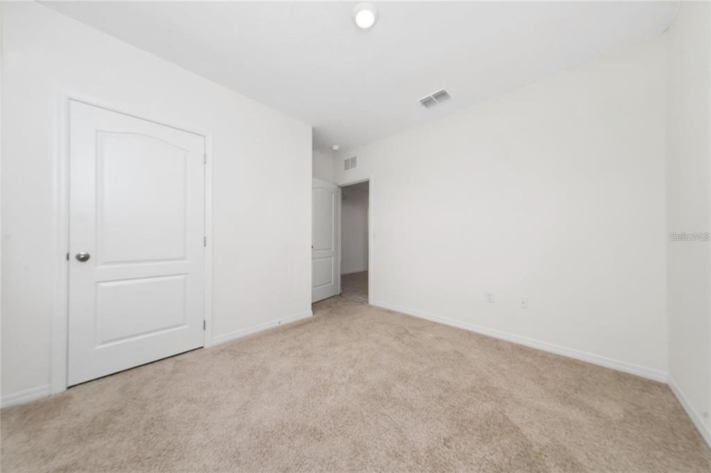 An empty bedroom features beige carpeting, white walls, and two white interior doors — 1213 RED HILL ROAD, DAVENPORT, FL